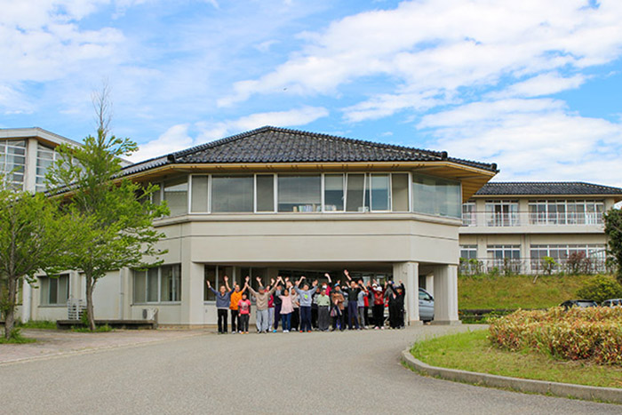 介護施設の建物外観。入居者とスタッフが玄関前に集合した風景